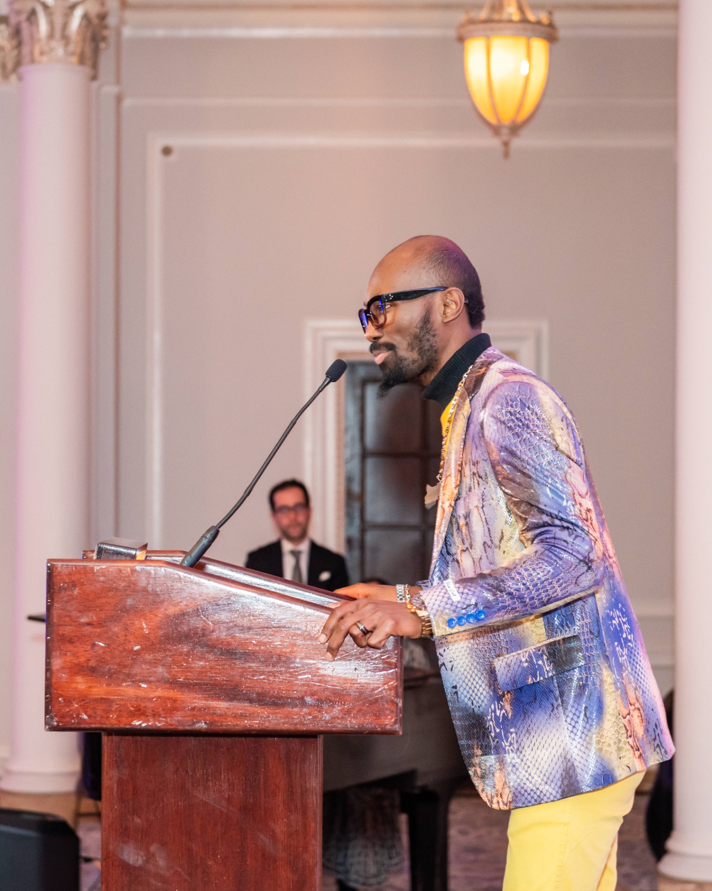 Speaker in iridescent jacket addressing guests from the Fairmont podium
