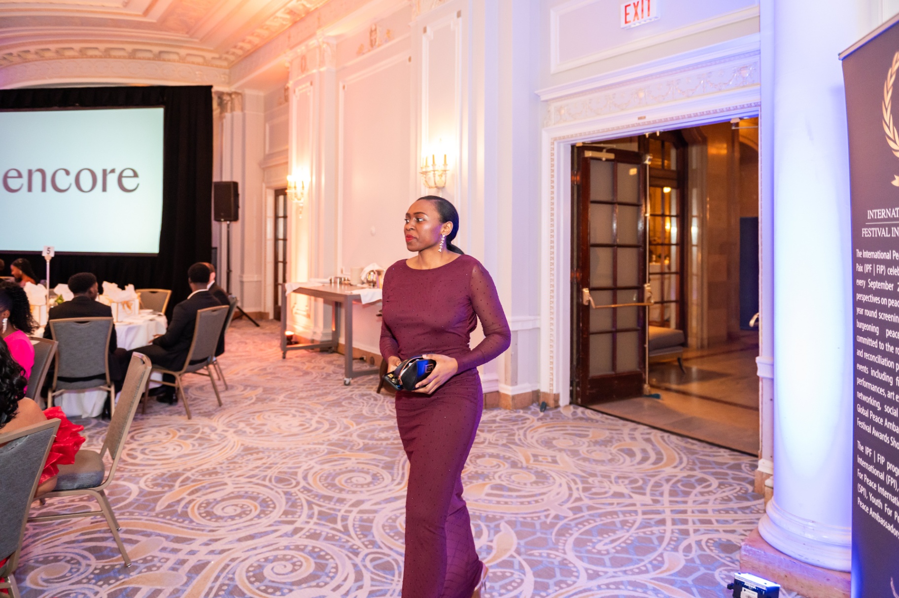 Guest in burgundy evening gown entering the ballroom past the International Peace Festival banner