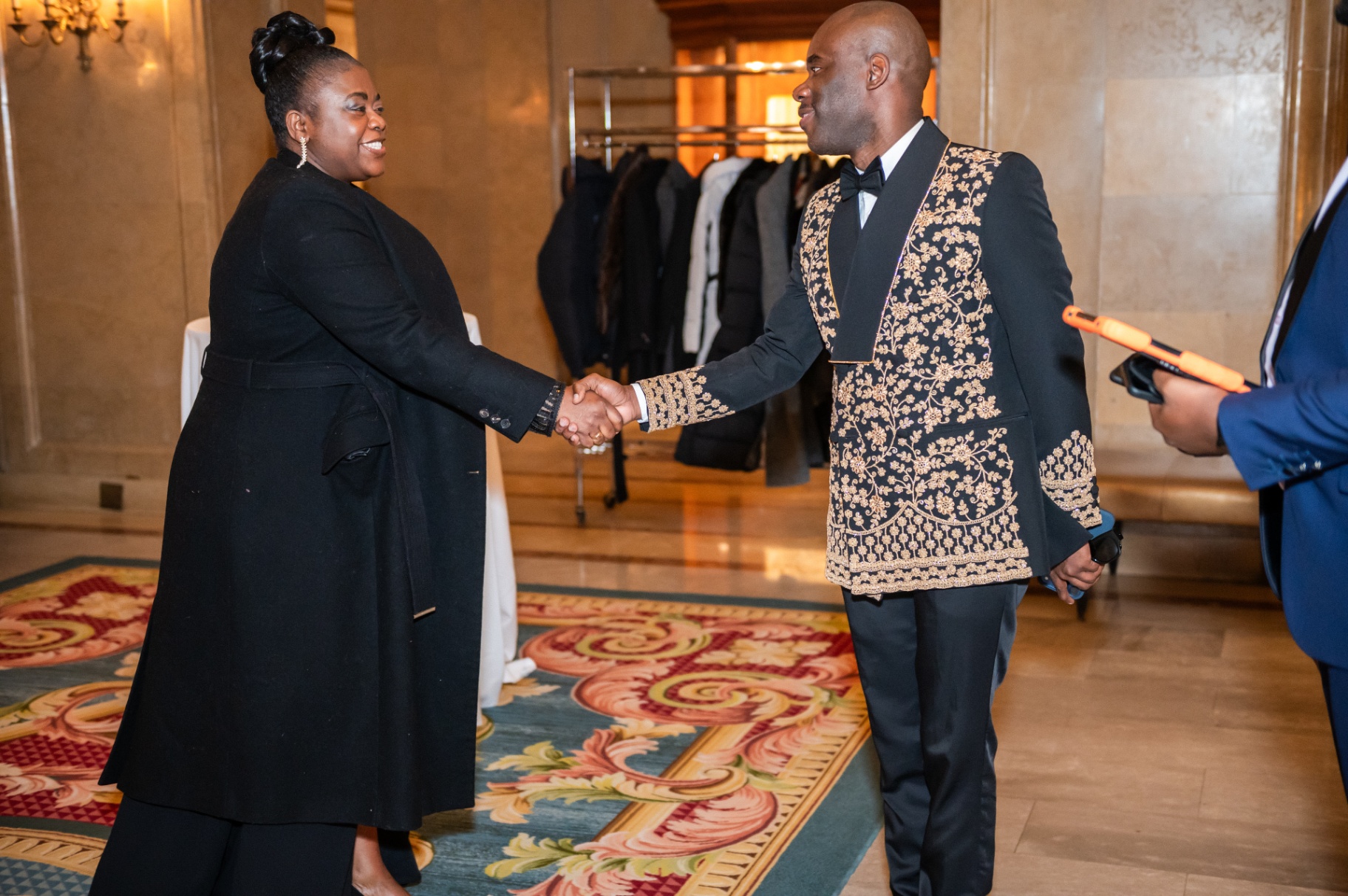 Guest greeting an attendee in embroidered black-and-gold formal wear