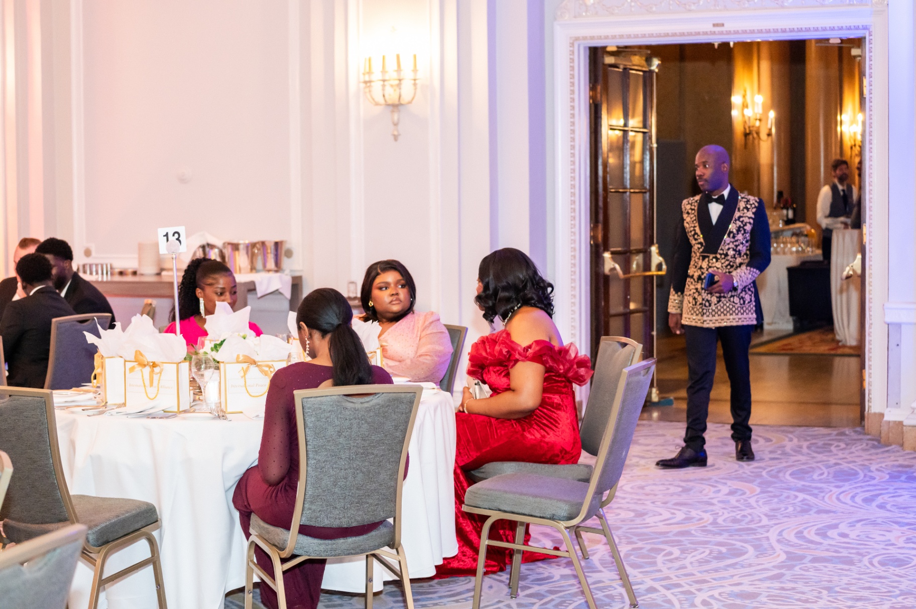 Gala attendees seated as a guest in patterned tuxedo enters the ballroom