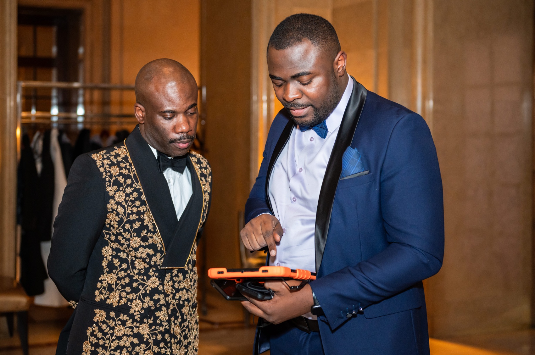 Two formally dressed guests reviewing a device together during the reception