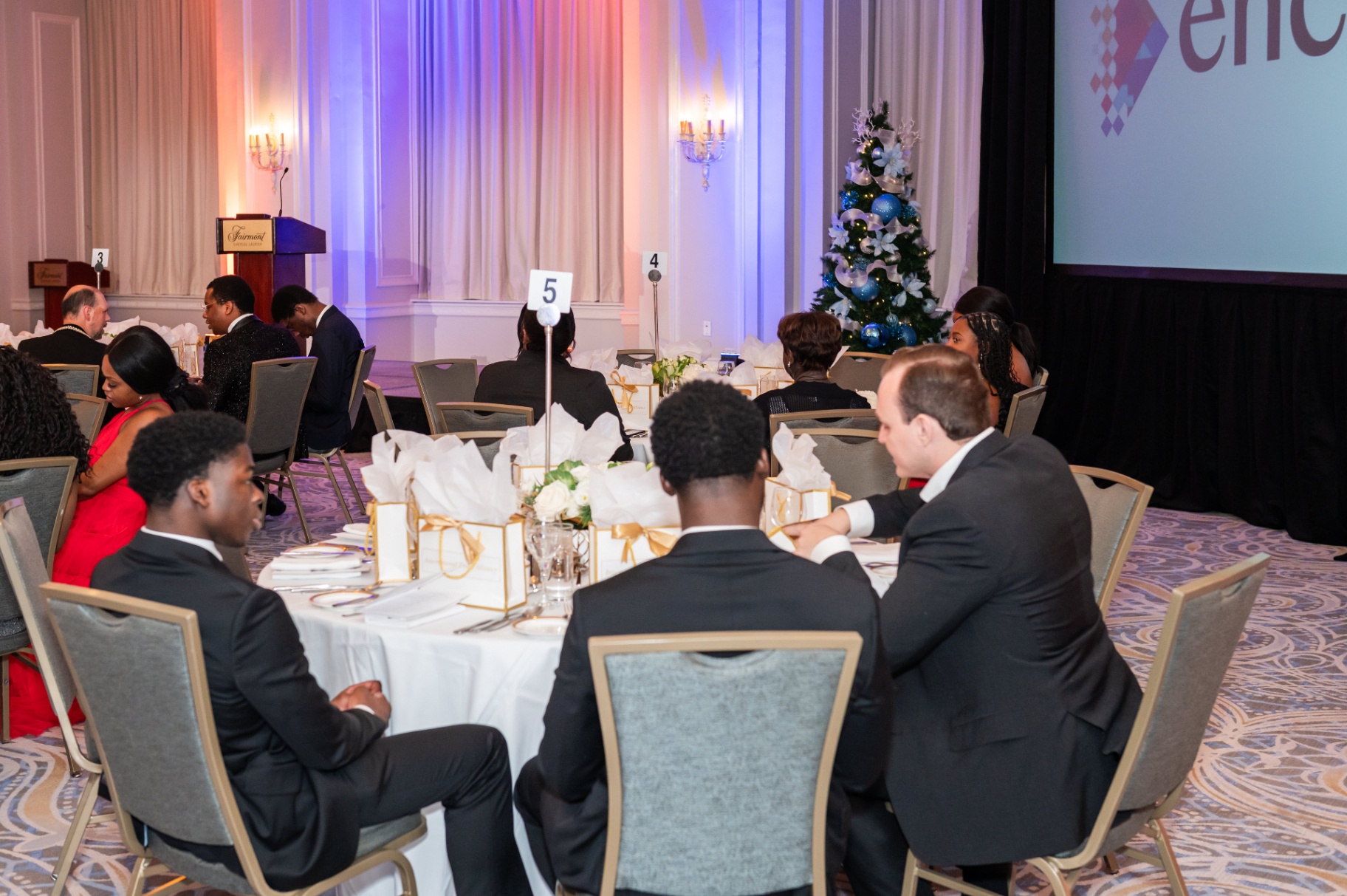 Guests seated at round tables facing the Fairmont stage and Encore screen